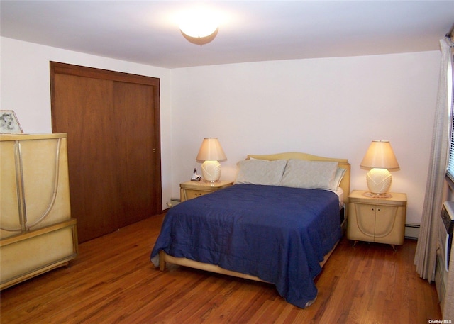 bedroom with dark wood-type flooring, baseboard heating, and a closet