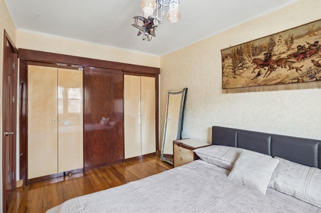 bedroom with dark wood-type flooring, ornamental molding, a closet, and a chandelier