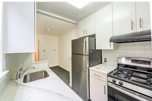 kitchen with light stone countertops, appliances with stainless steel finishes, white cabinetry, sink, and backsplash