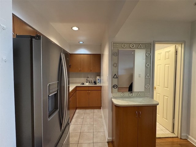 kitchen featuring kitchen peninsula, stainless steel refrigerator with ice dispenser, sink, light tile patterned flooring, and decorative backsplash