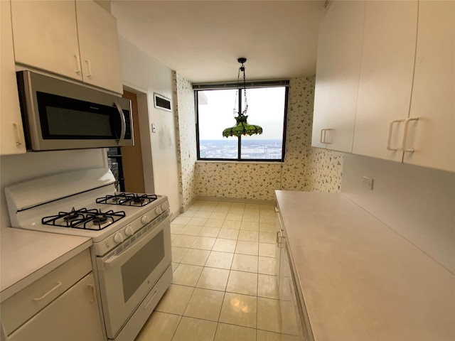 kitchen with white range with gas stovetop, pendant lighting, light tile patterned floors, and white cabinetry