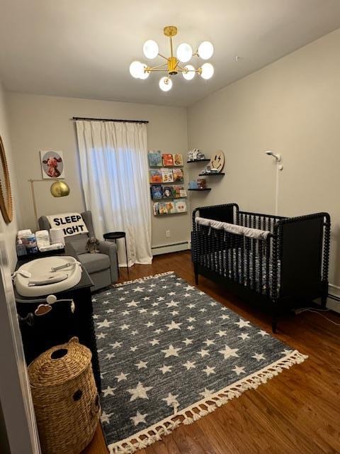 bedroom with dark wood-type flooring, a baseboard heating unit, a notable chandelier, and a crib