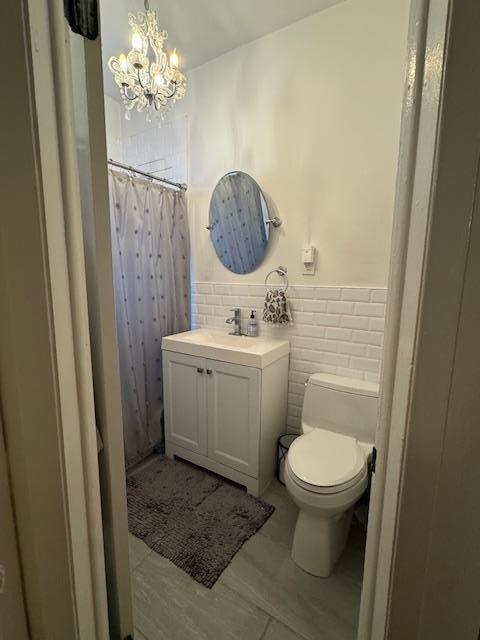 bathroom with tile walls, toilet, a notable chandelier, vanity, and a shower with shower curtain