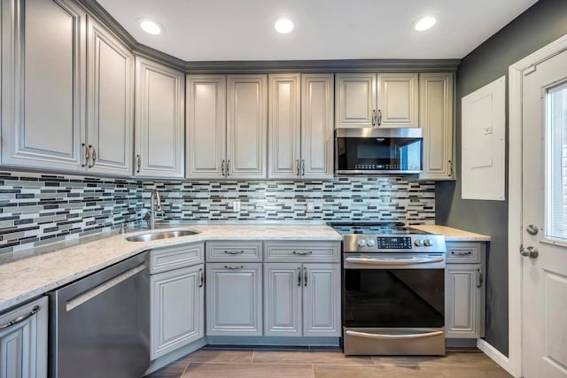 kitchen with sink, light stone countertops, gray cabinets, decorative backsplash, and stainless steel appliances