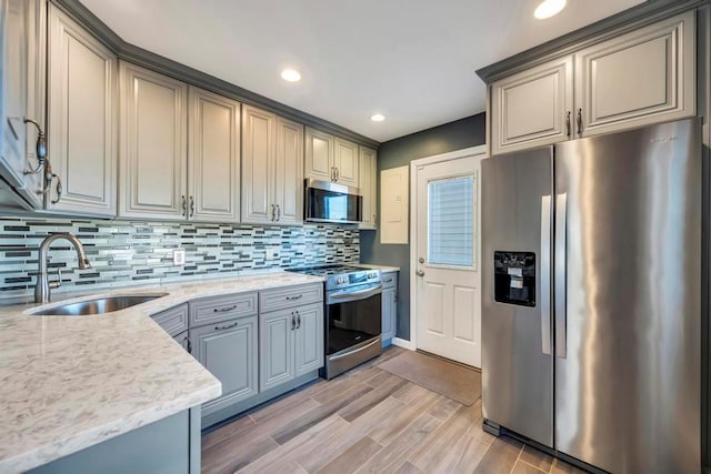 kitchen with appliances with stainless steel finishes, decorative backsplash, sink, gray cabinets, and light stone counters