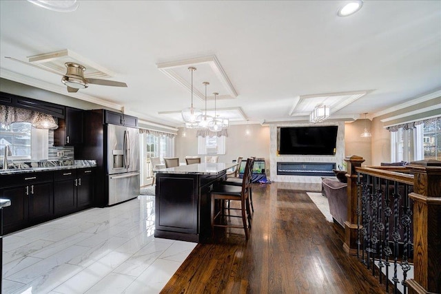 kitchen with crown molding, stainless steel fridge, a breakfast bar, a center island, and light stone counters