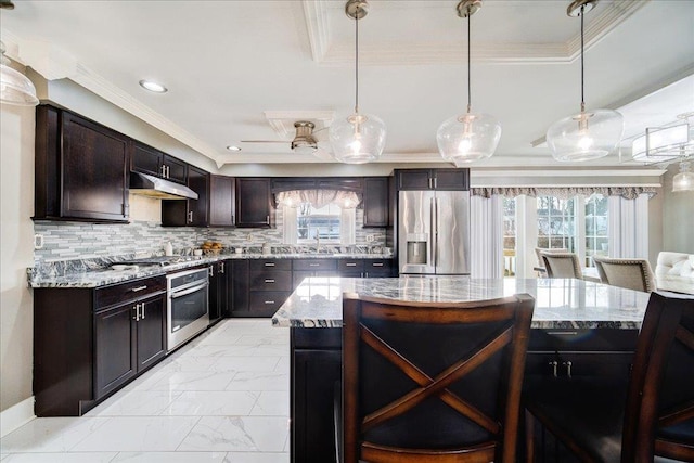 kitchen featuring dark brown cabinetry, a center island, hanging light fixtures, appliances with stainless steel finishes, and decorative backsplash