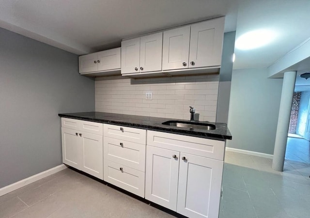 kitchen featuring backsplash, sink, light tile patterned flooring, white cabinets, and dark stone counters