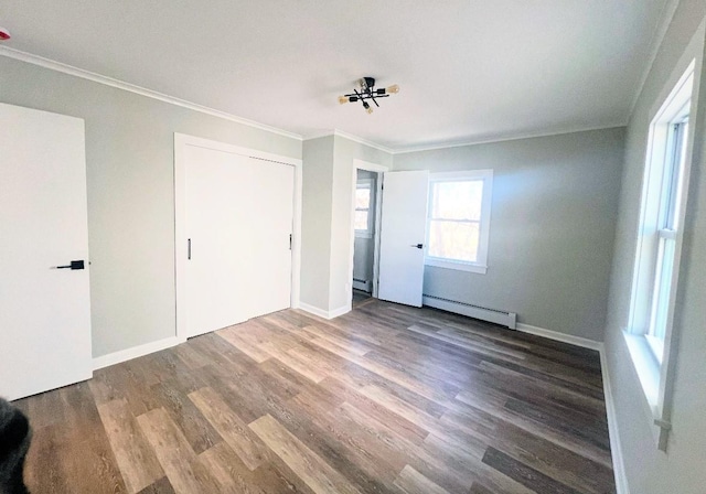 unfurnished bedroom featuring baseboard heating, a closet, hardwood / wood-style floors, and crown molding