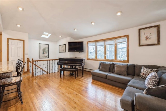 living room featuring vaulted ceiling with skylight and light hardwood / wood-style floors