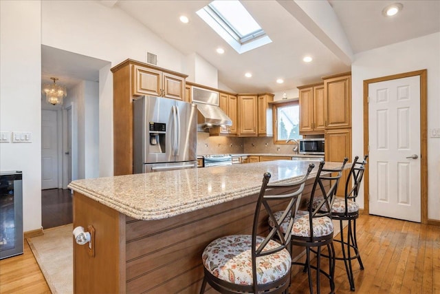 kitchen with vaulted ceiling with skylight, backsplash, appliances with stainless steel finishes, and a kitchen island