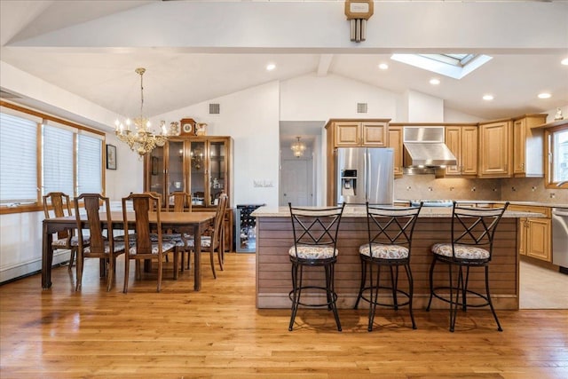 kitchen with stainless steel appliances, tasteful backsplash, hanging light fixtures, wall chimney exhaust hood, and a breakfast bar