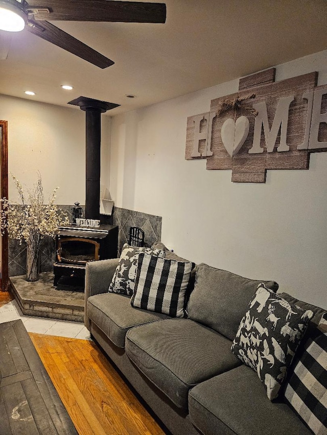 living room with light hardwood / wood-style flooring, ceiling fan, and a wood stove