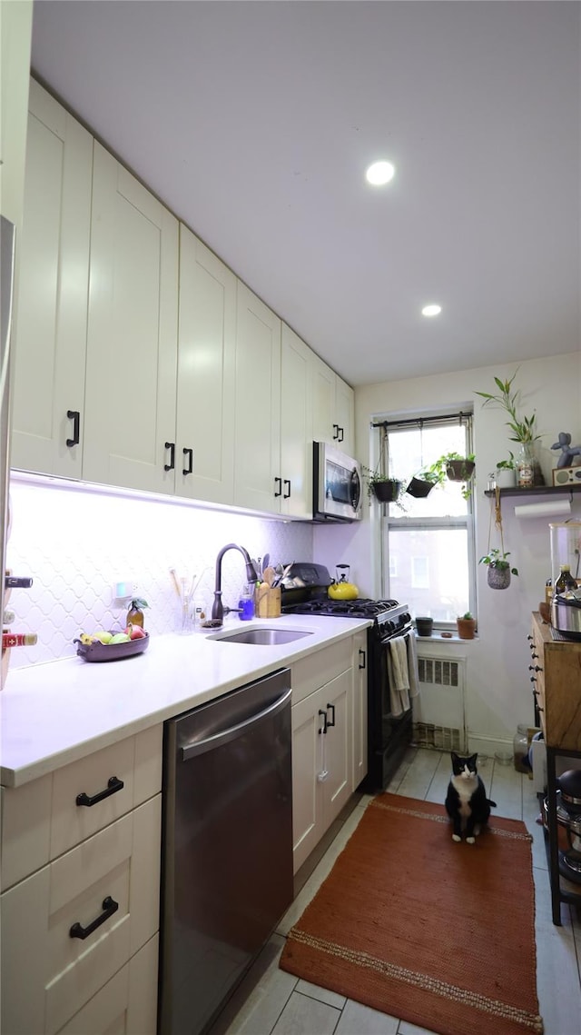 kitchen featuring light tile patterned floors, appliances with stainless steel finishes, radiator, white cabinets, and sink