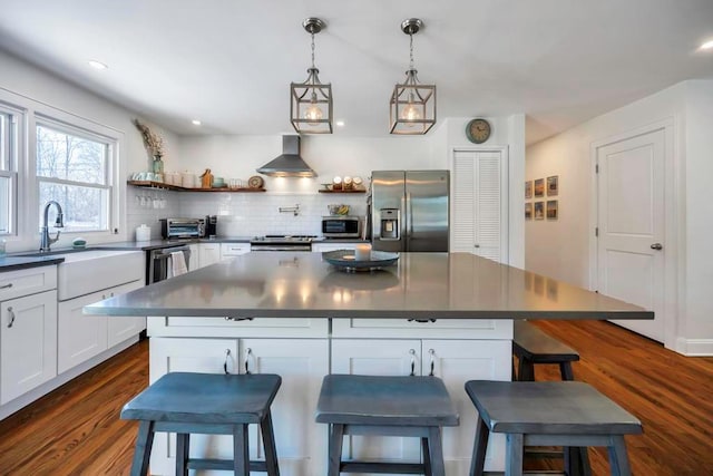 kitchen featuring appliances with stainless steel finishes, white cabinetry, decorative backsplash, a center island, and wall chimney exhaust hood