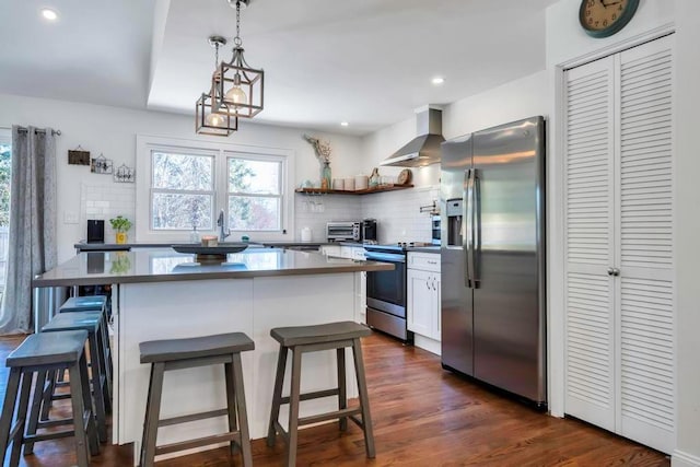 kitchen with wall chimney range hood, decorative backsplash, a breakfast bar, and appliances with stainless steel finishes