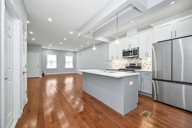 kitchen with a center island with sink, appliances with stainless steel finishes, hanging light fixtures, white cabinets, and sink