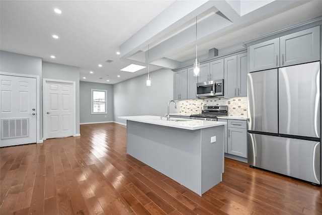 kitchen with stainless steel appliances, gray cabinetry, a kitchen island with sink, hanging light fixtures, and sink