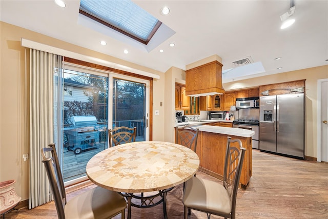 kitchen with light hardwood / wood-style floors, appliances with stainless steel finishes, a skylight, sink, and kitchen peninsula