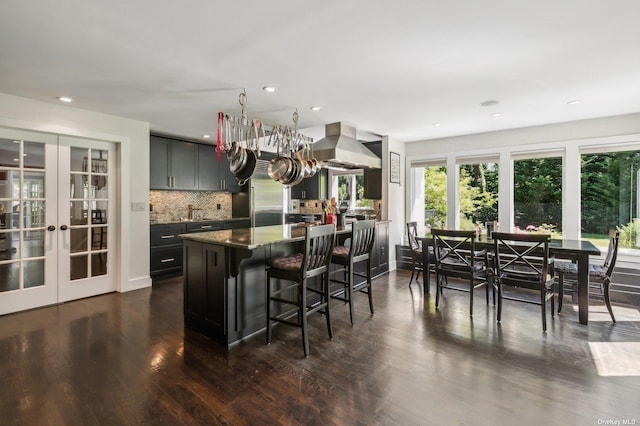 kitchen with tasteful backsplash, a kitchen breakfast bar, ventilation hood, french doors, and dark hardwood / wood-style flooring