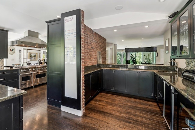 kitchen with backsplash, sink, island exhaust hood, dark wood-type flooring, and dark stone counters