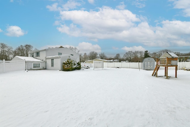 yard layered in snow featuring a playground and a storage shed