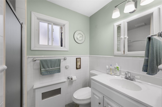 bathroom featuring radiator, a shower with door, tile walls, vanity, and toilet