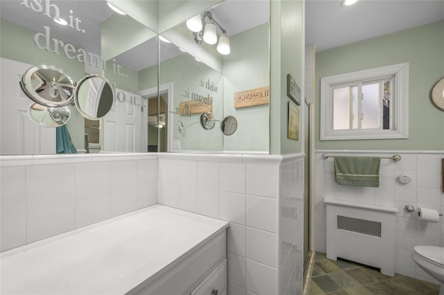 bathroom with tile walls, vanity, radiator heating unit, and toilet