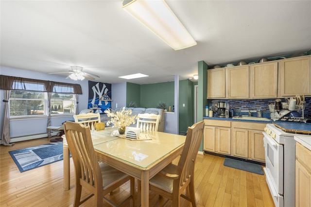 dining space with sink, ceiling fan, a baseboard heating unit, a skylight, and light wood-type flooring