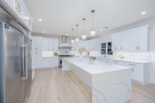 kitchen with white cabinets, premium appliances, wall chimney range hood, and a kitchen island