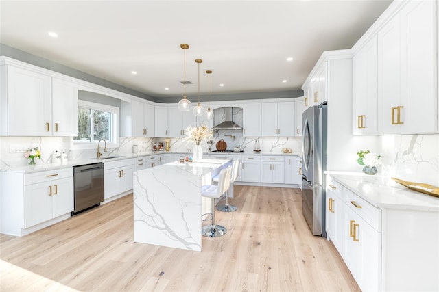 kitchen featuring white cabinets, appliances with stainless steel finishes, wall chimney exhaust hood, hanging light fixtures, and a kitchen island with sink