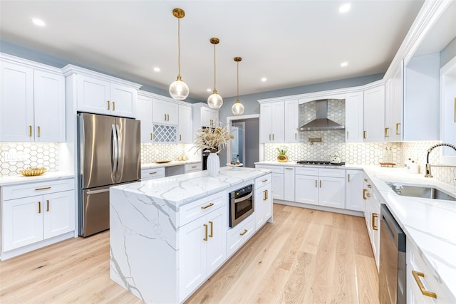 kitchen featuring white cabinets, appliances with stainless steel finishes, wall chimney exhaust hood, decorative light fixtures, and sink