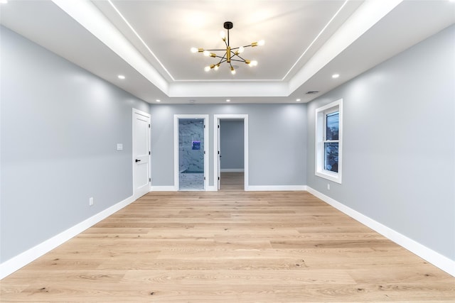 empty room featuring a notable chandelier, a tray ceiling, and light hardwood / wood-style flooring