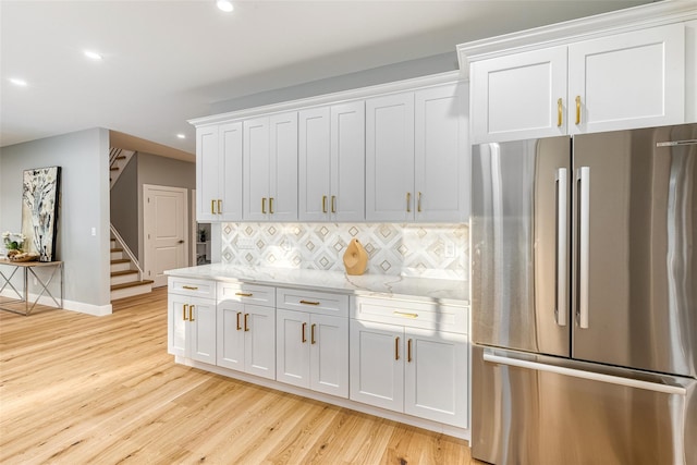 kitchen featuring white cabinetry, backsplash, light wood-type flooring, stainless steel refrigerator, and light stone counters