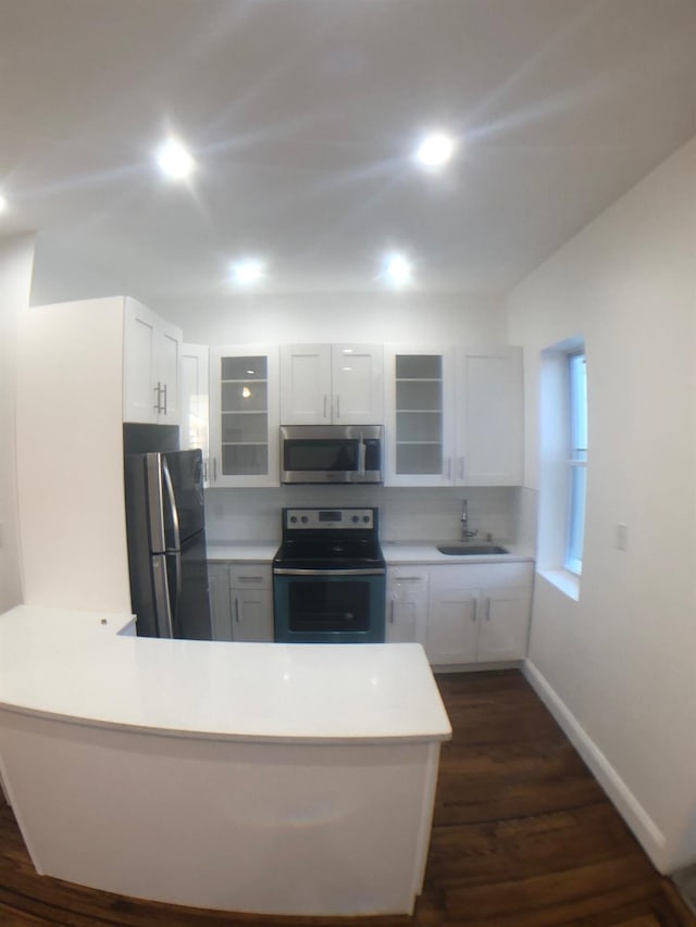 kitchen featuring appliances with stainless steel finishes, white cabinetry, dark hardwood / wood-style flooring, sink, and kitchen peninsula