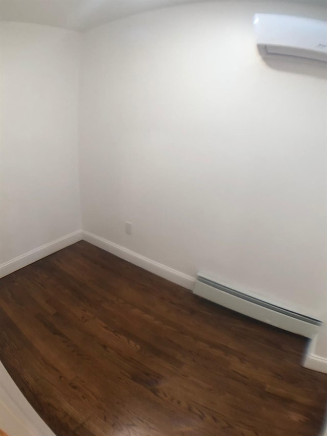 unfurnished room with baseboard heating, dark hardwood / wood-style flooring, and a wall mounted air conditioner