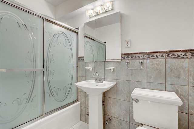 full bathroom featuring sink, combined bath / shower with glass door, toilet, and tile walls