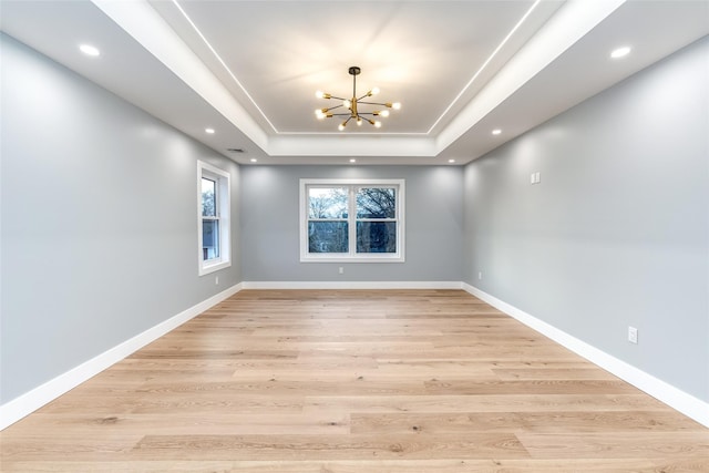 spare room featuring a chandelier, light hardwood / wood-style floors, and a tray ceiling