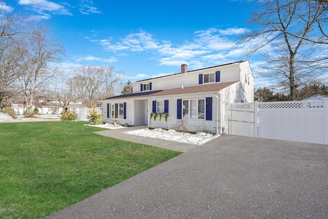 view of front of house with driveway, a shingled roof, a chimney, fence, and a front lawn