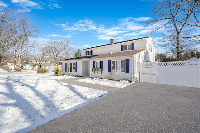 view of front of property with aphalt driveway, fence, a chimney, and a shingled roof