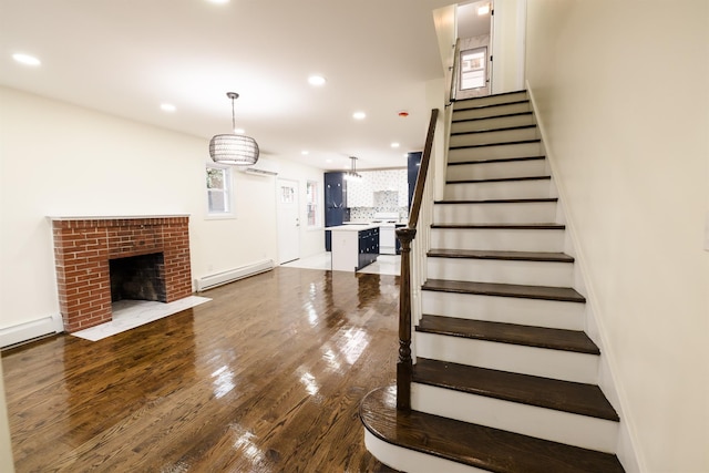 stairs featuring a brick fireplace, a baseboard radiator, and hardwood / wood-style flooring