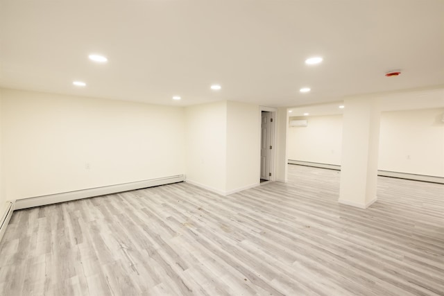 basement with baseboard heating, a wall unit AC, and light hardwood / wood-style floors