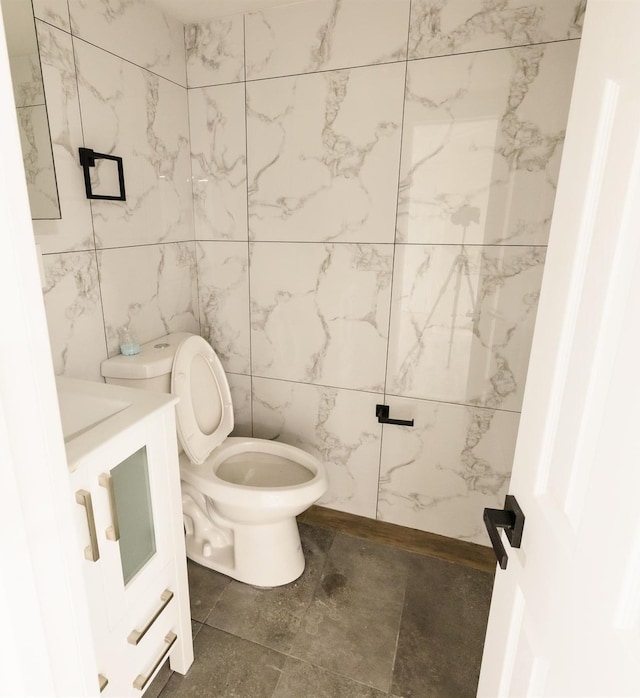 bathroom featuring toilet, vanity, and tile walls