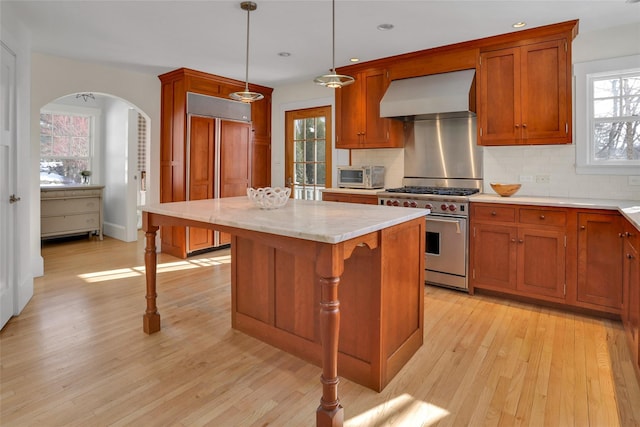 kitchen featuring wall chimney exhaust hood, high end appliances, hanging light fixtures, light wood-type flooring, and a kitchen island