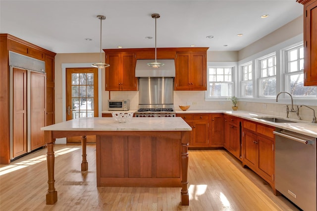 kitchen with a kitchen island, appliances with stainless steel finishes, sink, hanging light fixtures, and wall chimney exhaust hood