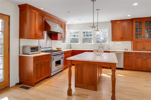 kitchen featuring a breakfast bar area, hanging light fixtures, stainless steel appliances, a center island, and wall chimney exhaust hood