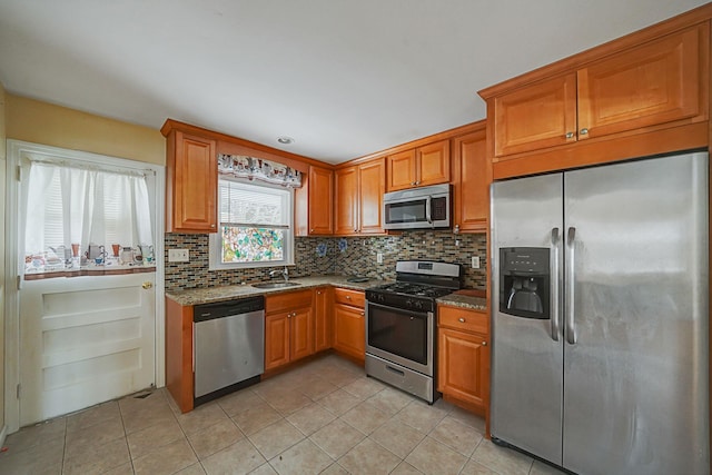 kitchen with light stone countertops, appliances with stainless steel finishes, decorative backsplash, and sink