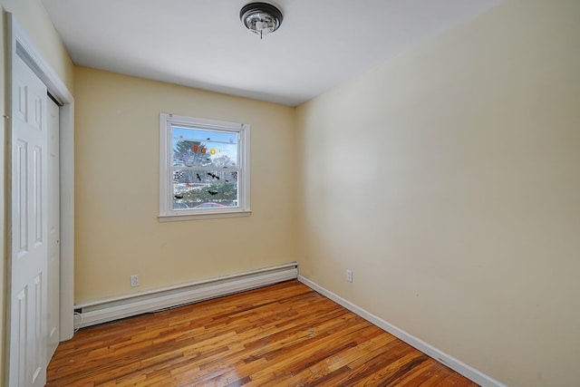 unfurnished bedroom featuring wood-type flooring, a baseboard heating unit, and a closet