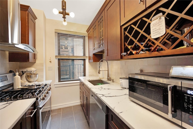 kitchen featuring wall chimney range hood, stainless steel appliances, sink, backsplash, and light stone counters