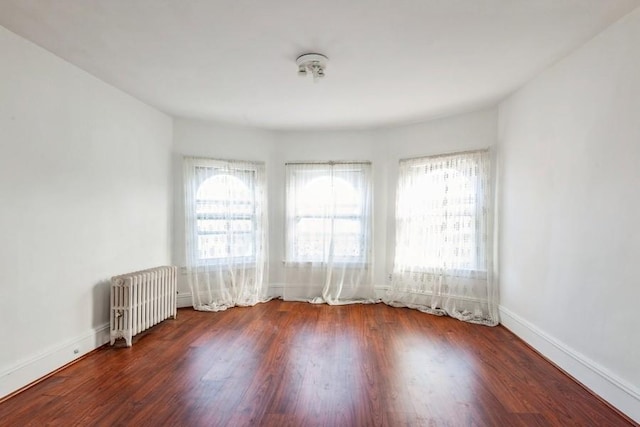 empty room featuring dark hardwood / wood-style floors, radiator, and a healthy amount of sunlight